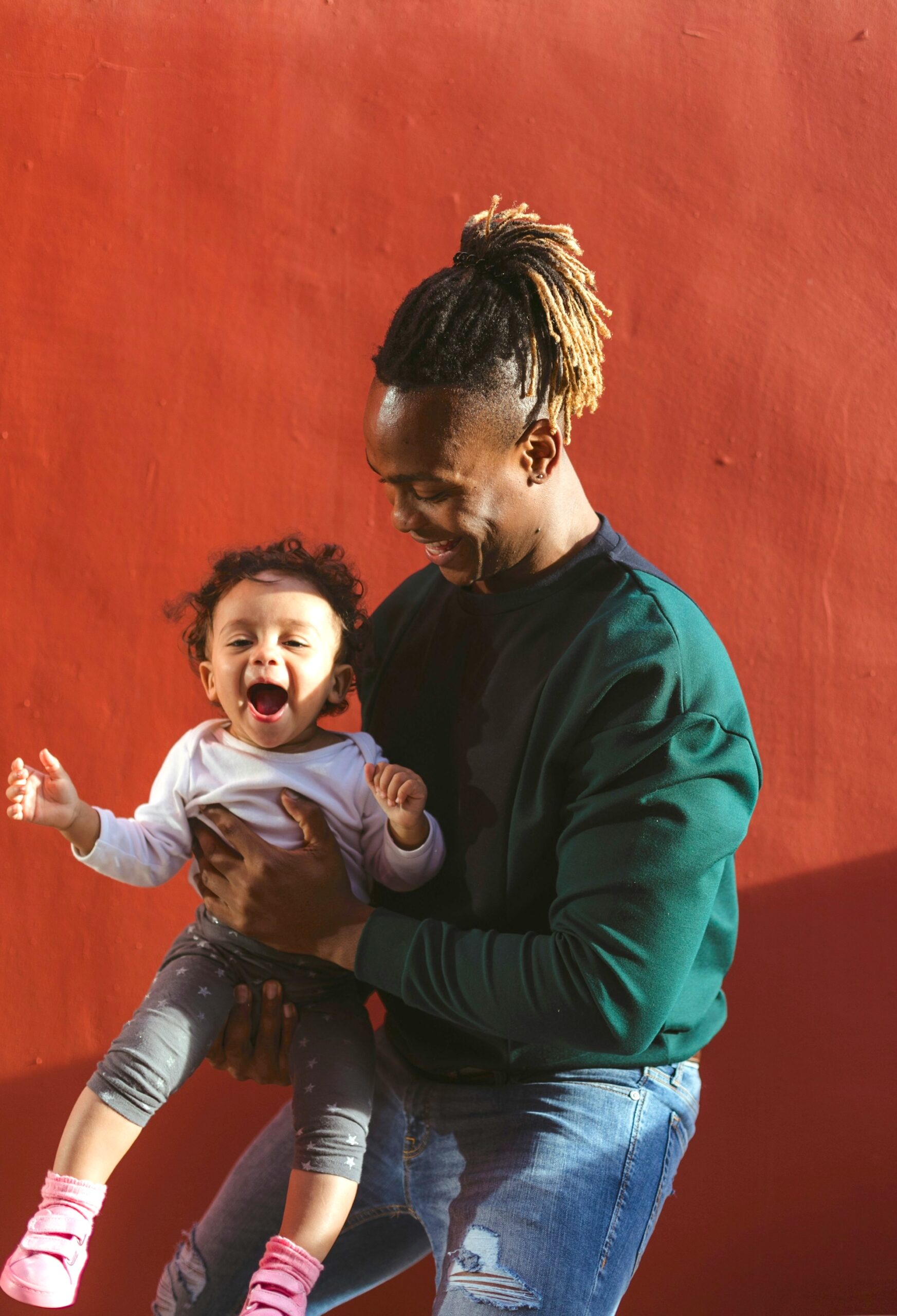 Father holding child in front of a red wall.